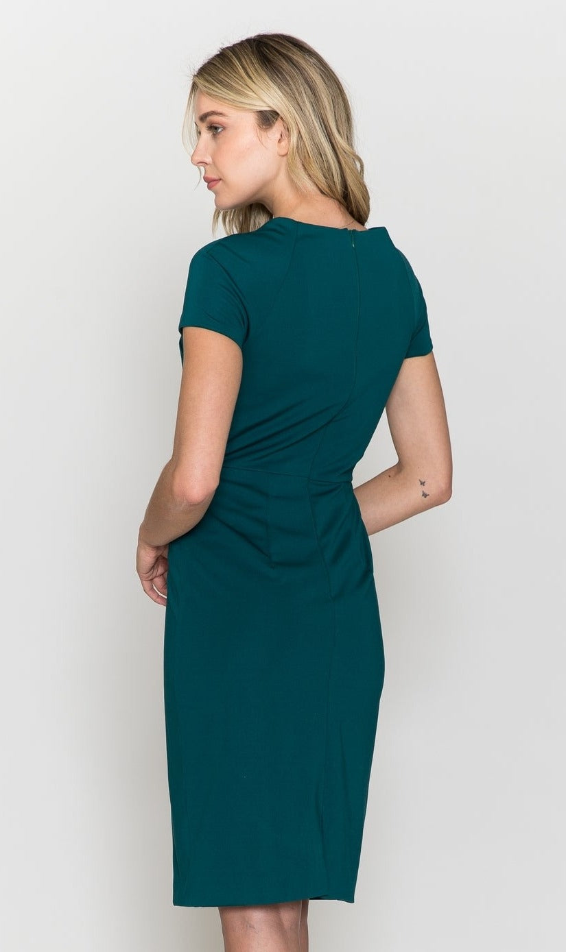 A woman with blonde hair, wearing the Short Sleeve Knee-Length Semi-Formal Dress 8774 in teal, stands facing away with her head turned to the side against a plain light background.